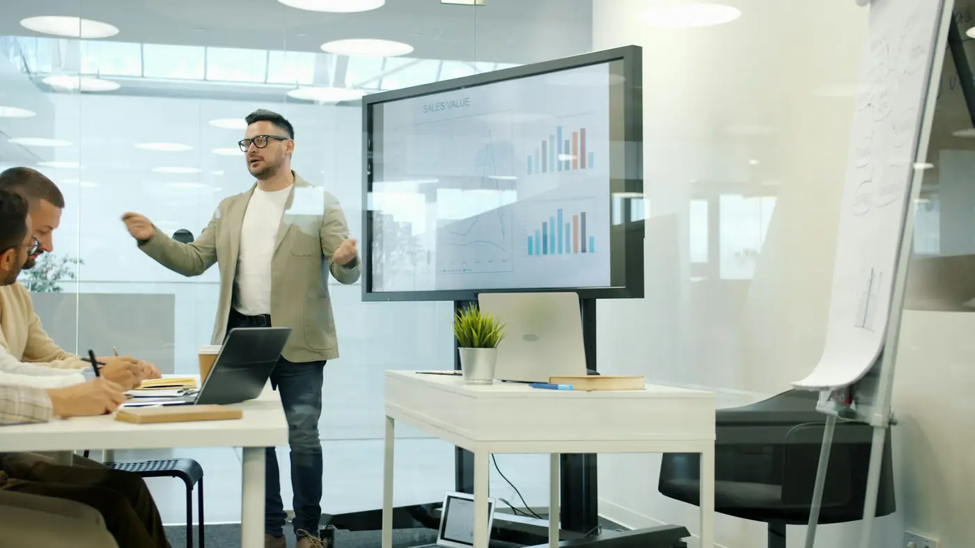 A consultant presenting charts on a large screen to a small team in a meeting room