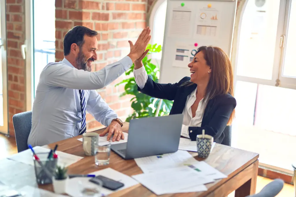 Two people shaking hands across a table in a meeting